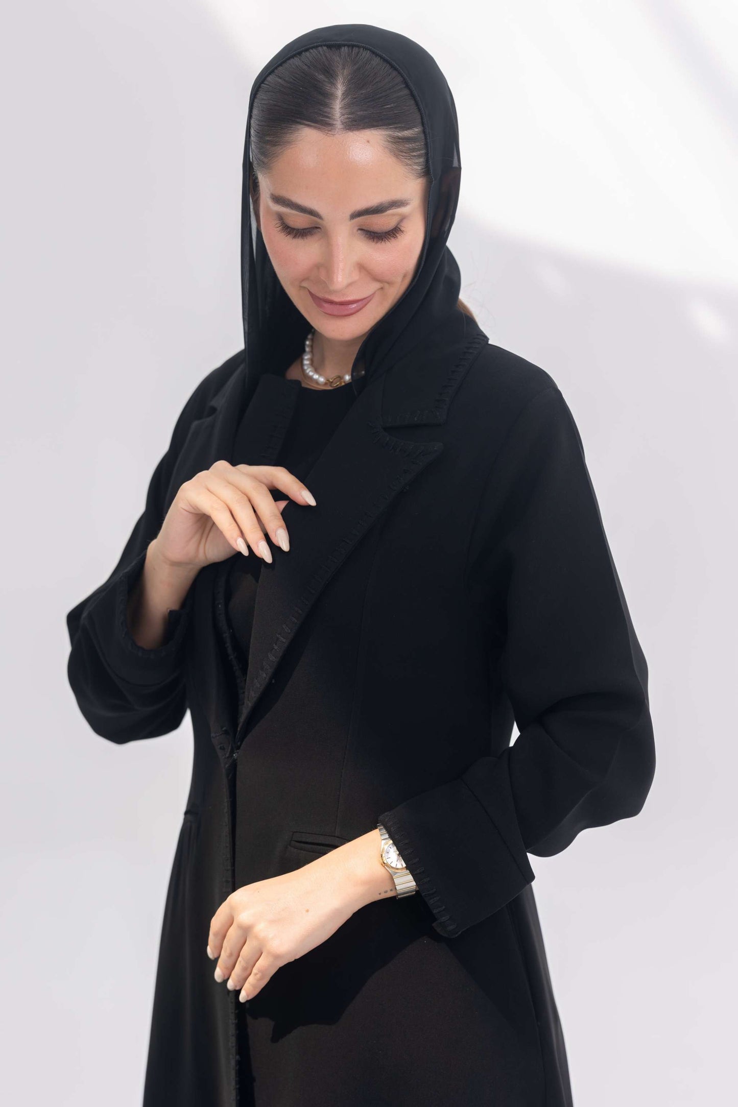 Woman wearing sophisticated black crepe blazer abaya with tailored silhouette and intricate black embroidery.