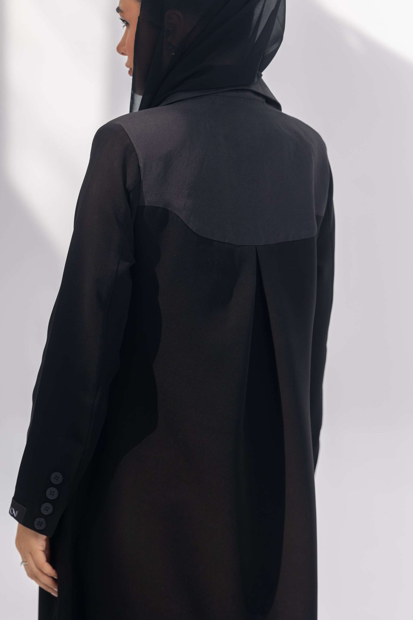 Black crepe abaya with dark grey fabric accents and sleek silhouette worn with a black hijab