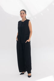 Woman wearing inner muse-black crepe sleeveless vest and matching wide-leg pants in a minimalist setting