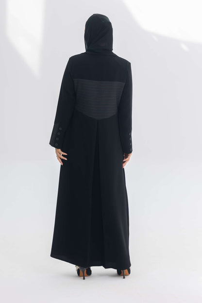 Woman wearing black crepe blazer abaya with contrasting back panel detail, standing against white background