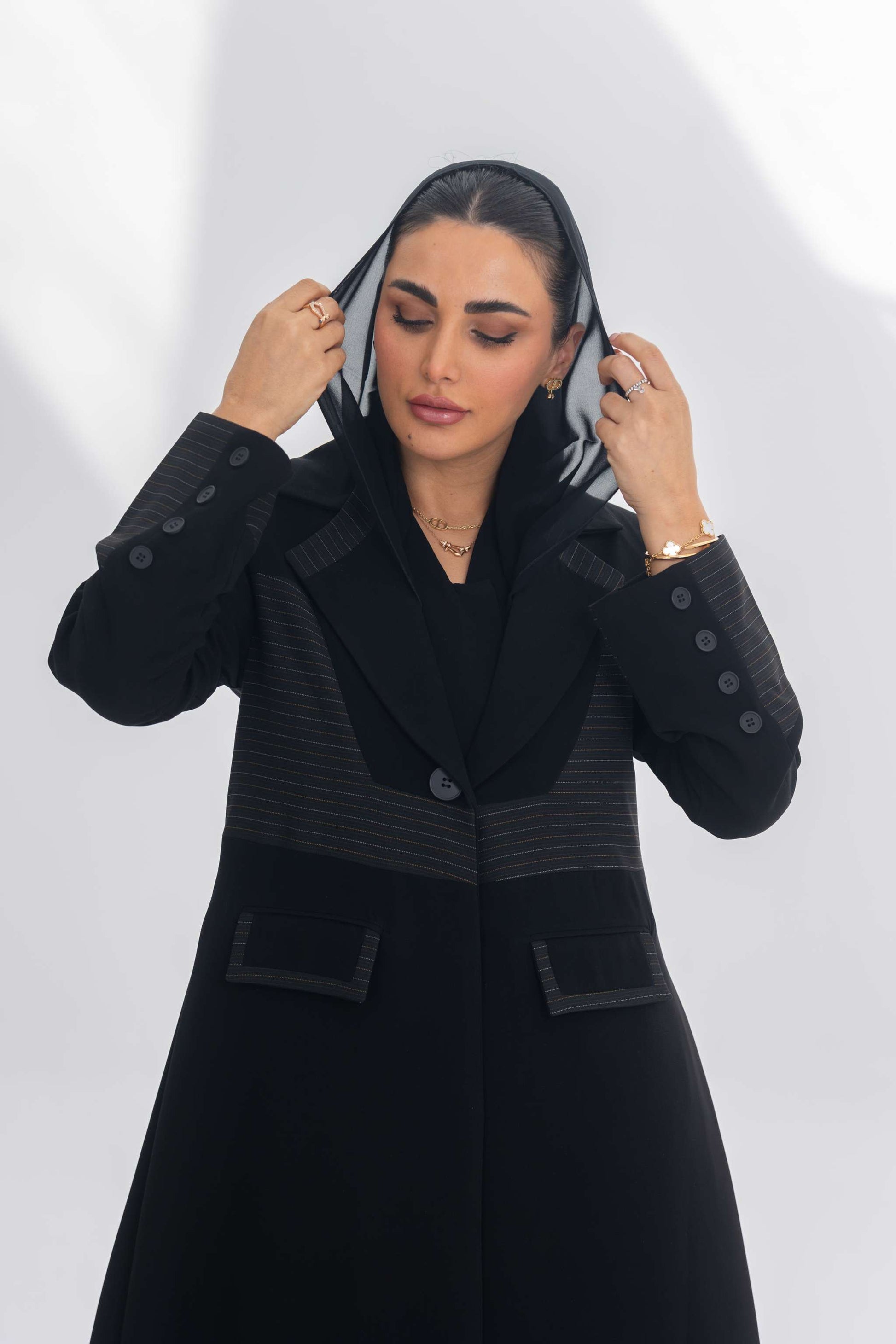 Black crepe blazer abaya with contrasting fabric detail, worn by woman adjusting hood, showcasing elegant modern design.