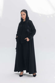 Woman wearing Noira Belle black crepe abaya with striped satin panels and hood.