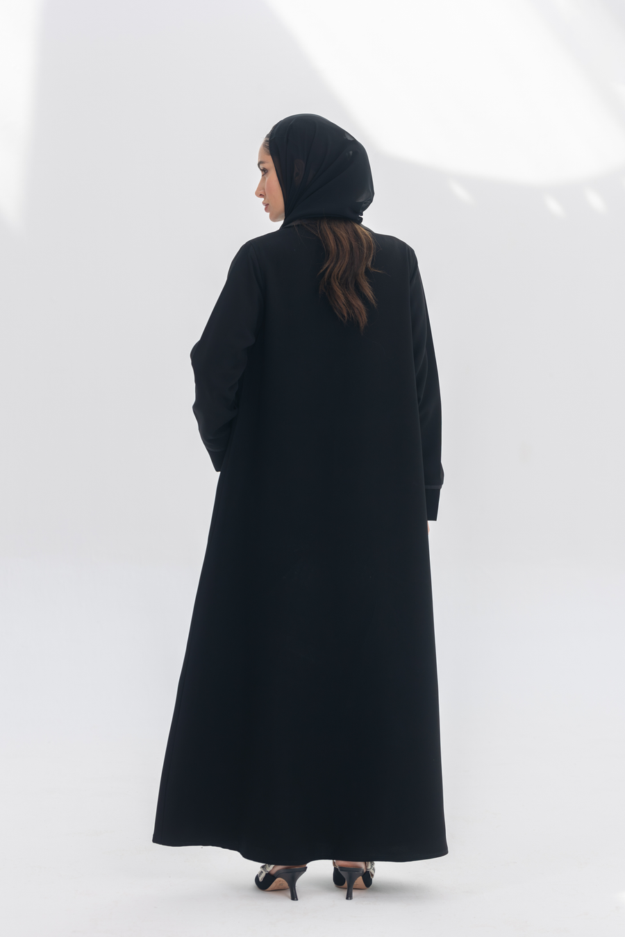Back view of Noira Belle black crepe abaya with striped satin panels worn by woman in black hijab and heels