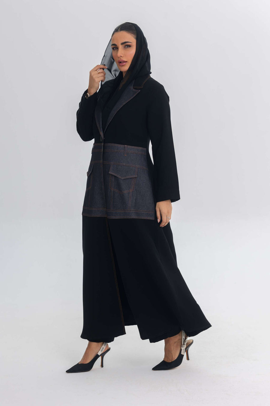 Woman wearing Blue Stitch black crepe abaya with denim fabric details and blue stitching, styled with black heels and a black headscarf.