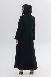 Back view of a woman wearing a sleek black crepe abaya with a hood, part of the Blue Stitch collection.