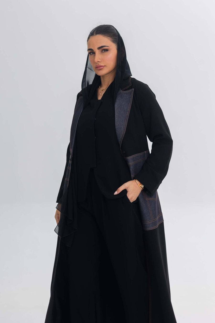 Woman wearing sleek black crepe abaya with edgy denim blue stitch detailing and modern design