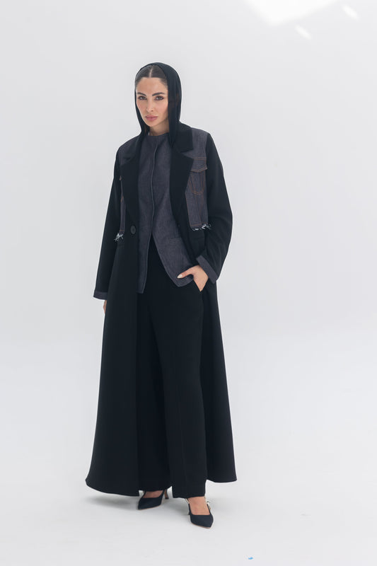 Woman wearing Denim Veil black crepe abaya with denim accents and headscarf, posing on white background