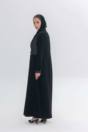 Woman wearing black crepe abaya with denim accents and black hijab, styled for modern modest fashion.