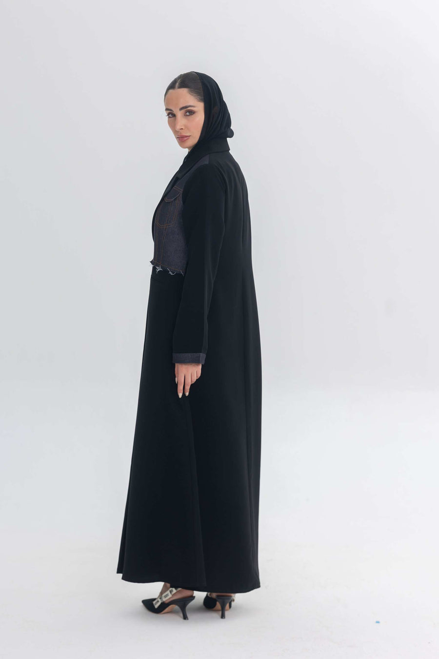 Woman wearing black crepe abaya with denim accents and black hijab, styled for modern modest fashion.