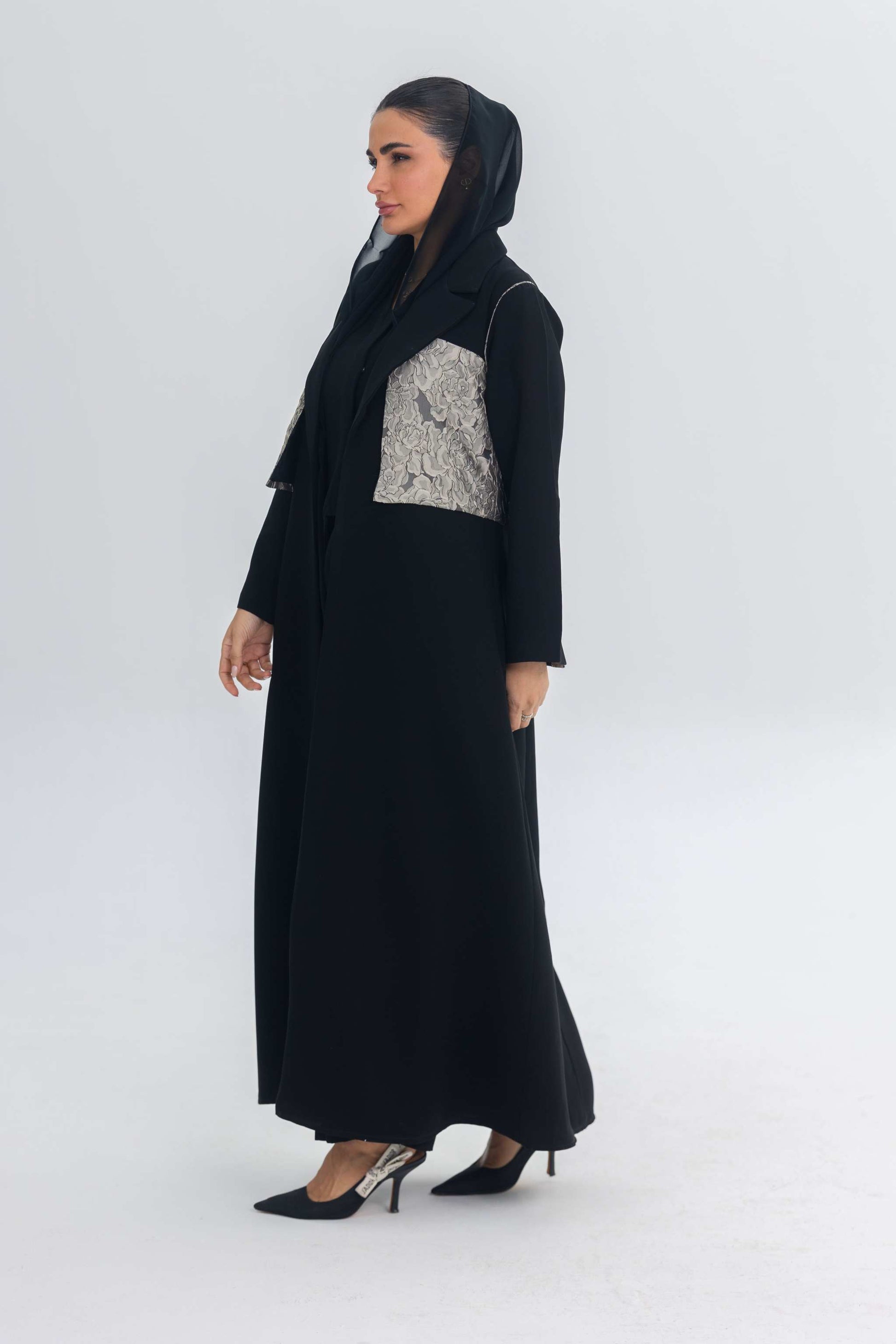 Elegant black crepe abaya with jacquard panel detail worn by woman in black heels and headscarf