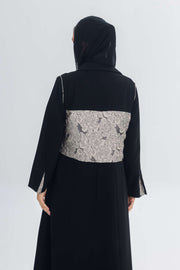 Back view of black crepe abaya featuring a textured jacquard panel and long sleeves with slit detailing.