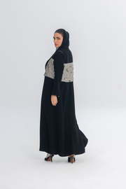 Elegant black crepe abaya with textured jacquard panel, worn by woman in heels and headscarf, showcasing flowing and sophisticated design