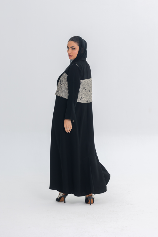 Elegant black crepe abaya with textured jacquard panel, worn by woman in heels and headscarf, showcasing flowing and sophisticated design