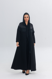 Woman wearing a black satin and crepe abaya with lace detailing, standing against a plain background.