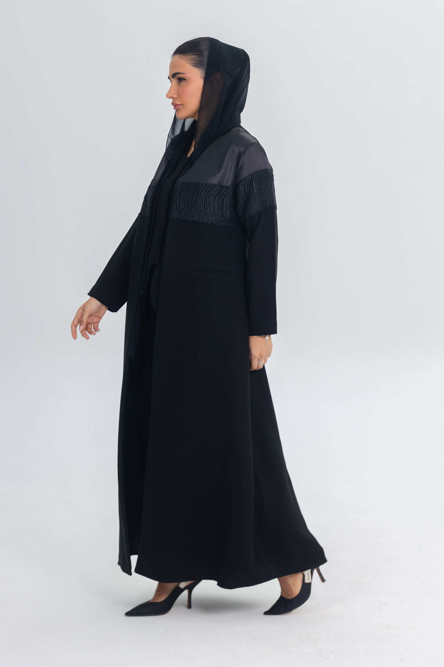 Elegant black satin and crepe abaya with lace detailing and hood worn by woman in heels