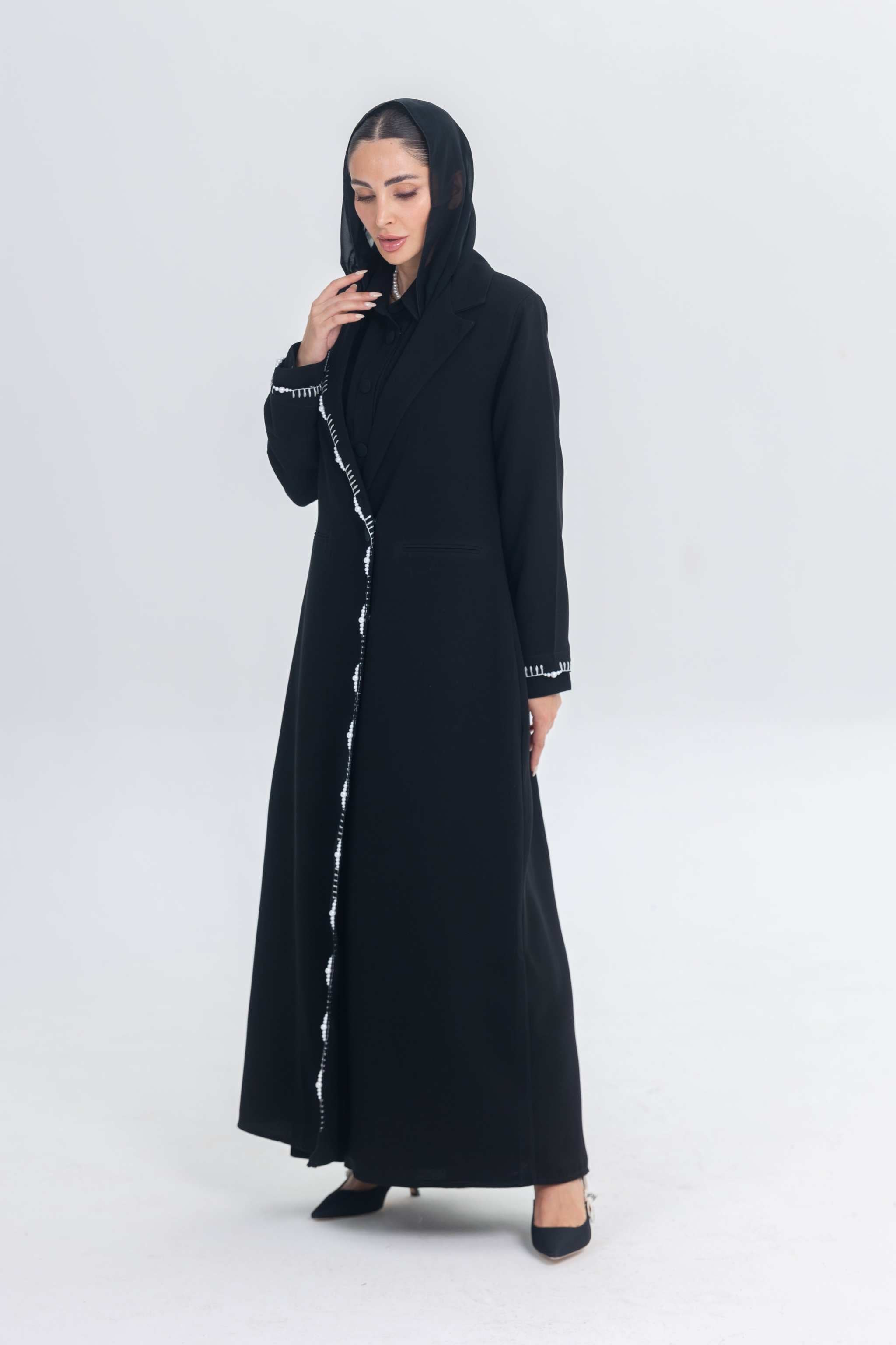 Black crepe blazer abaya with white pearl and bead embroidery, tailored silhouette, worn by a woman with a headscarf and black heels.