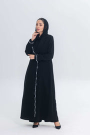 Black crepe blazer abaya with white pearl and bead embroidery, tailored silhouette, hand-stitched embellishments, worn by woman with hood.