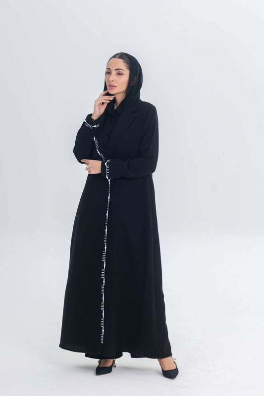 Black crepe blazer abaya with white pearl and bead embroidery, tailored silhouette, hand-stitched embellishments, worn by woman with hood.
