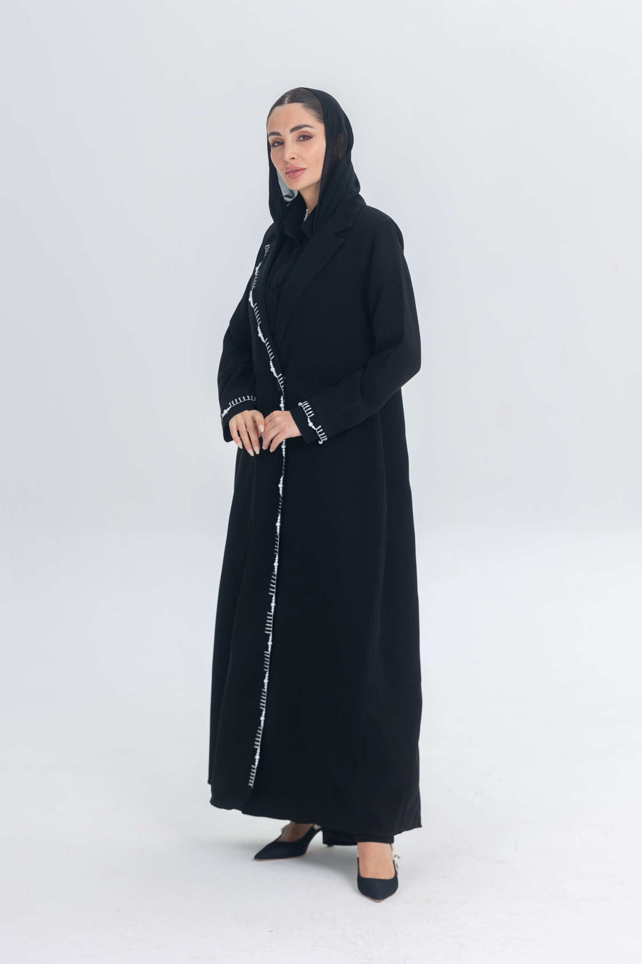 Black crepe blazer abaya with white pearl and bead embroidery, tailored silhouette, worn by woman in black heels and headscarf
