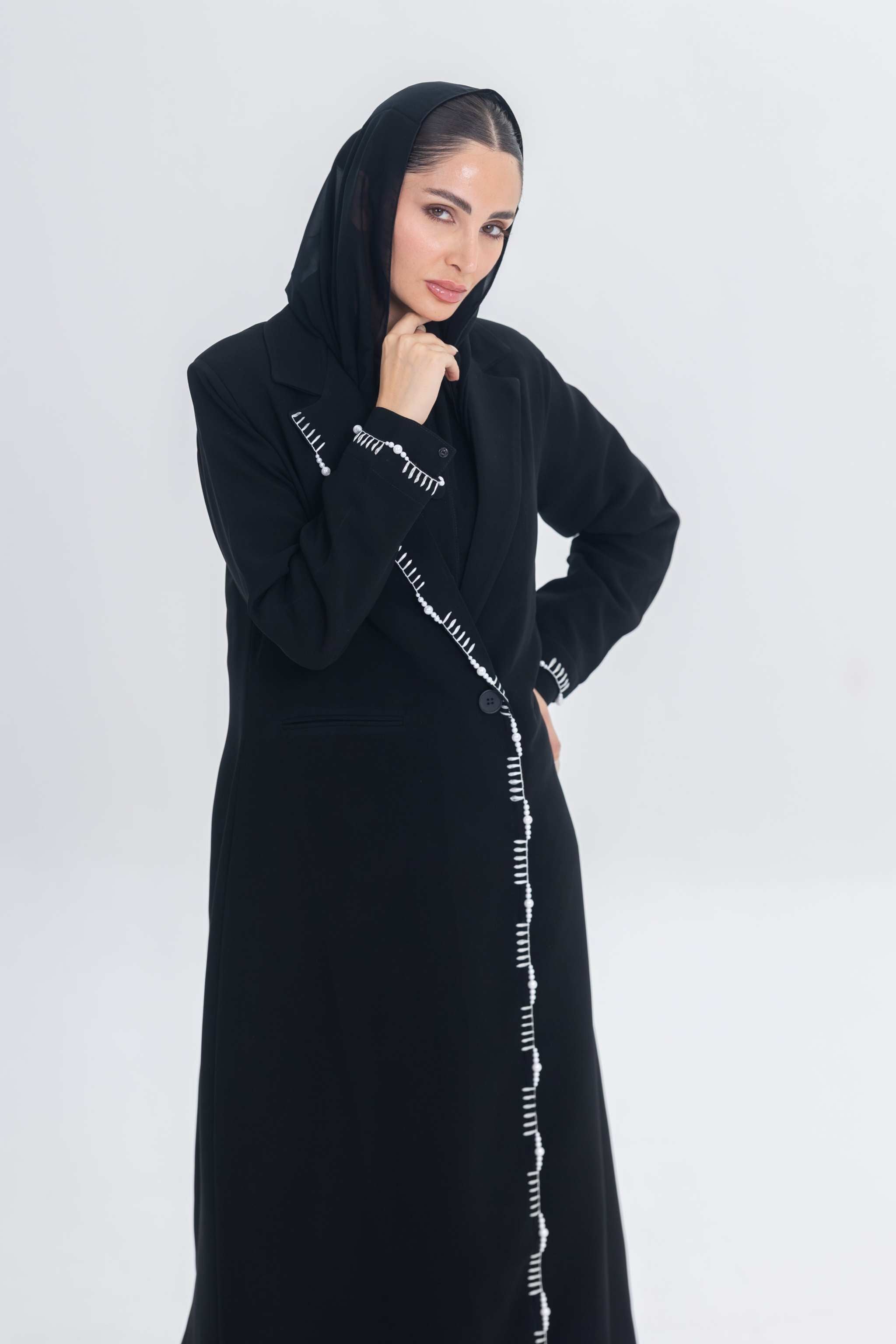 Woman wearing black crepe blazer abaya with white pearl and bead embroidery detailing.