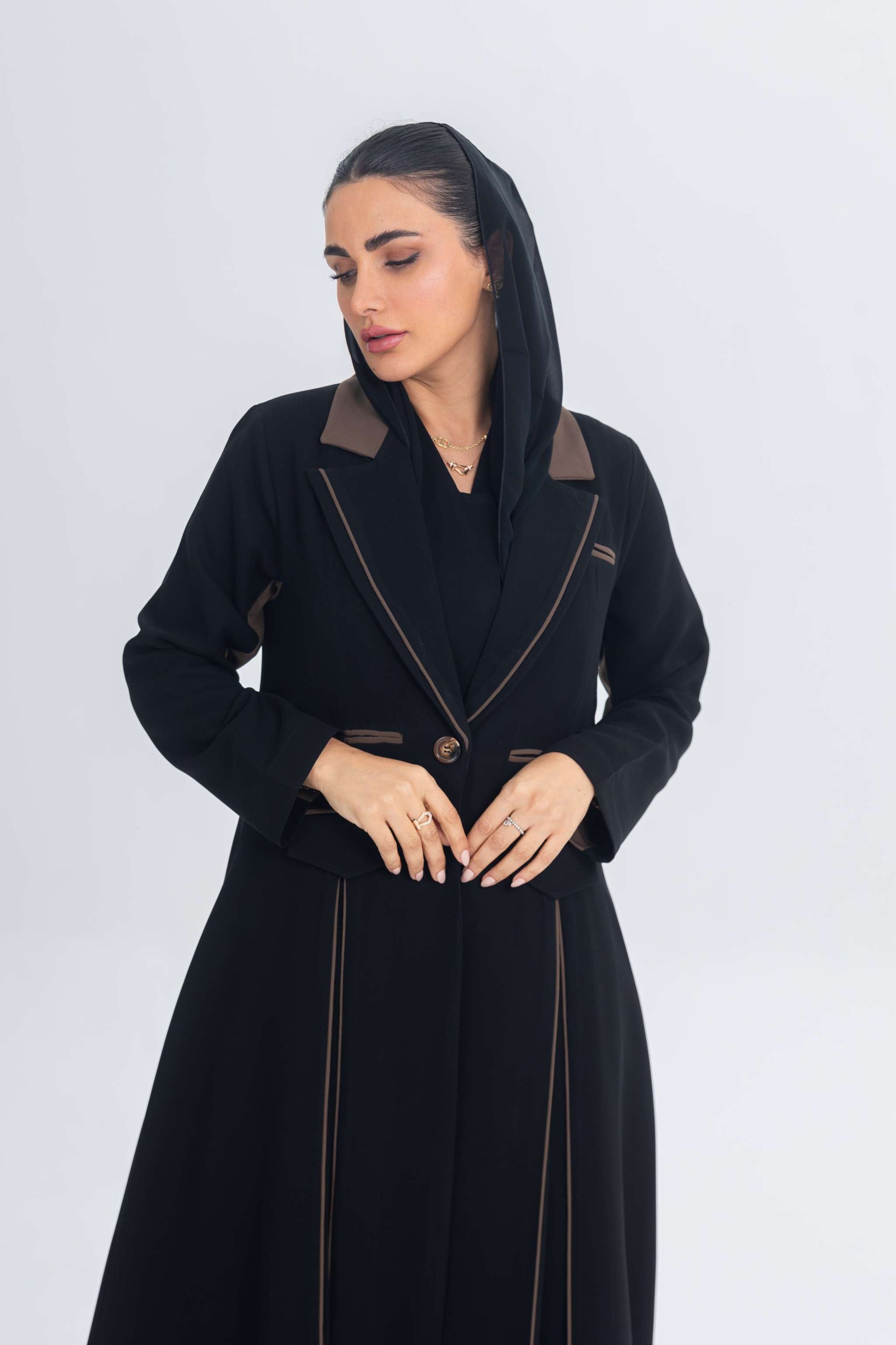 Black crepe blazer abaya with brown detailing and refined chestnut glow accents, styled on a woman with a sleek silhouette.