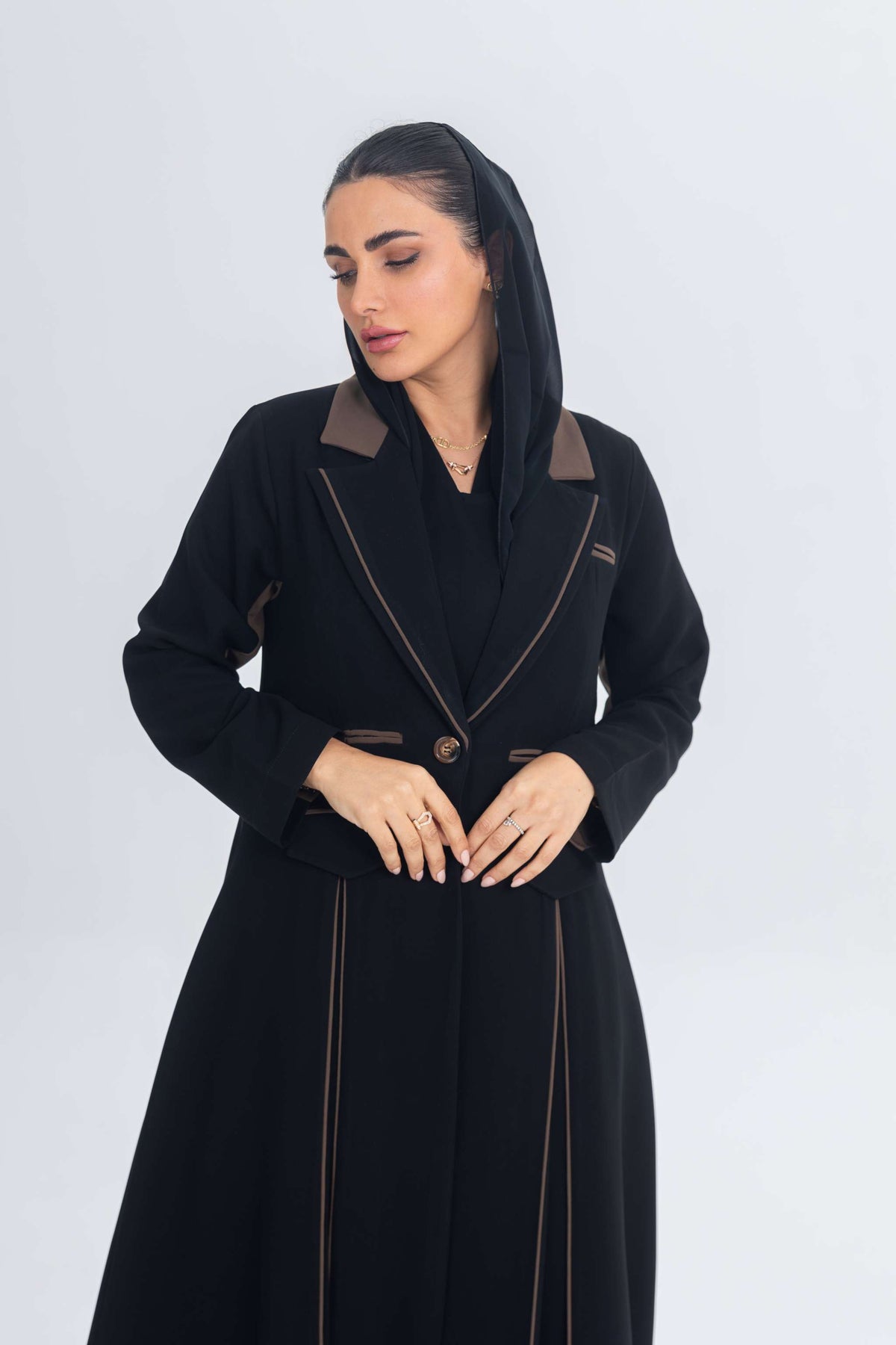 Black crepe blazer abaya with brown detailing and refined chestnut glow accents, styled on a woman with a sleek silhouette.