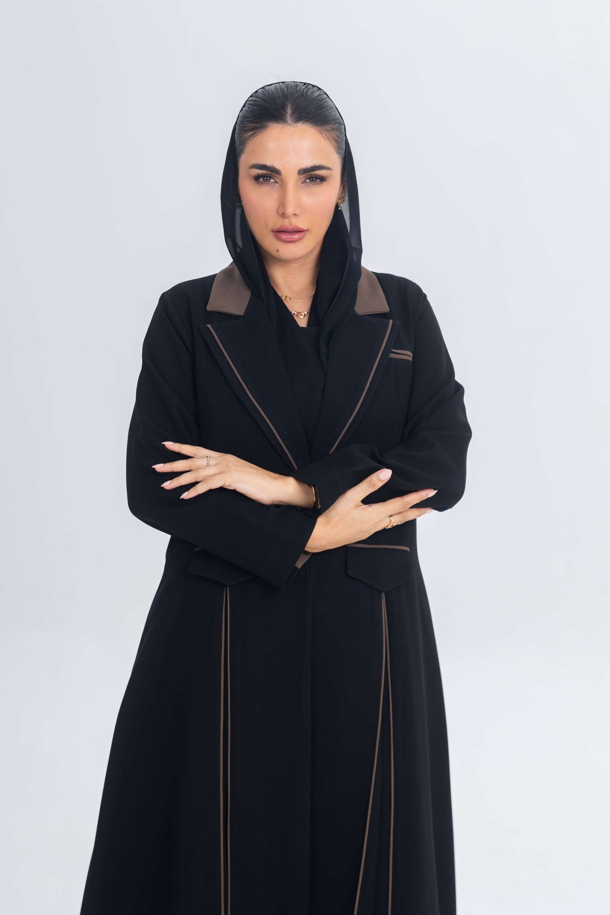 Woman wearing black crepe blazer abaya with brown trims and detailing, posing against white background