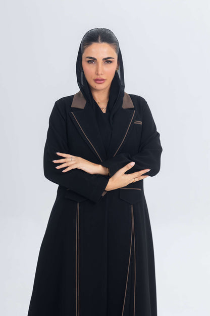 Woman wearing black crepe blazer abaya with brown trims and detailing, posing against white background