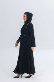 Woman wearing black crepe blazer abaya with chestnut brown trim and detailing, styled with matching hood and heels.