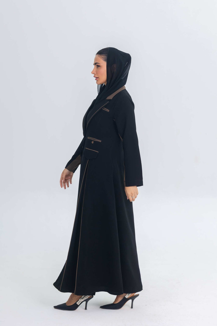 Woman wearing black crepe blazer abaya with chestnut brown trim and detailing, styled with matching hood and heels.
