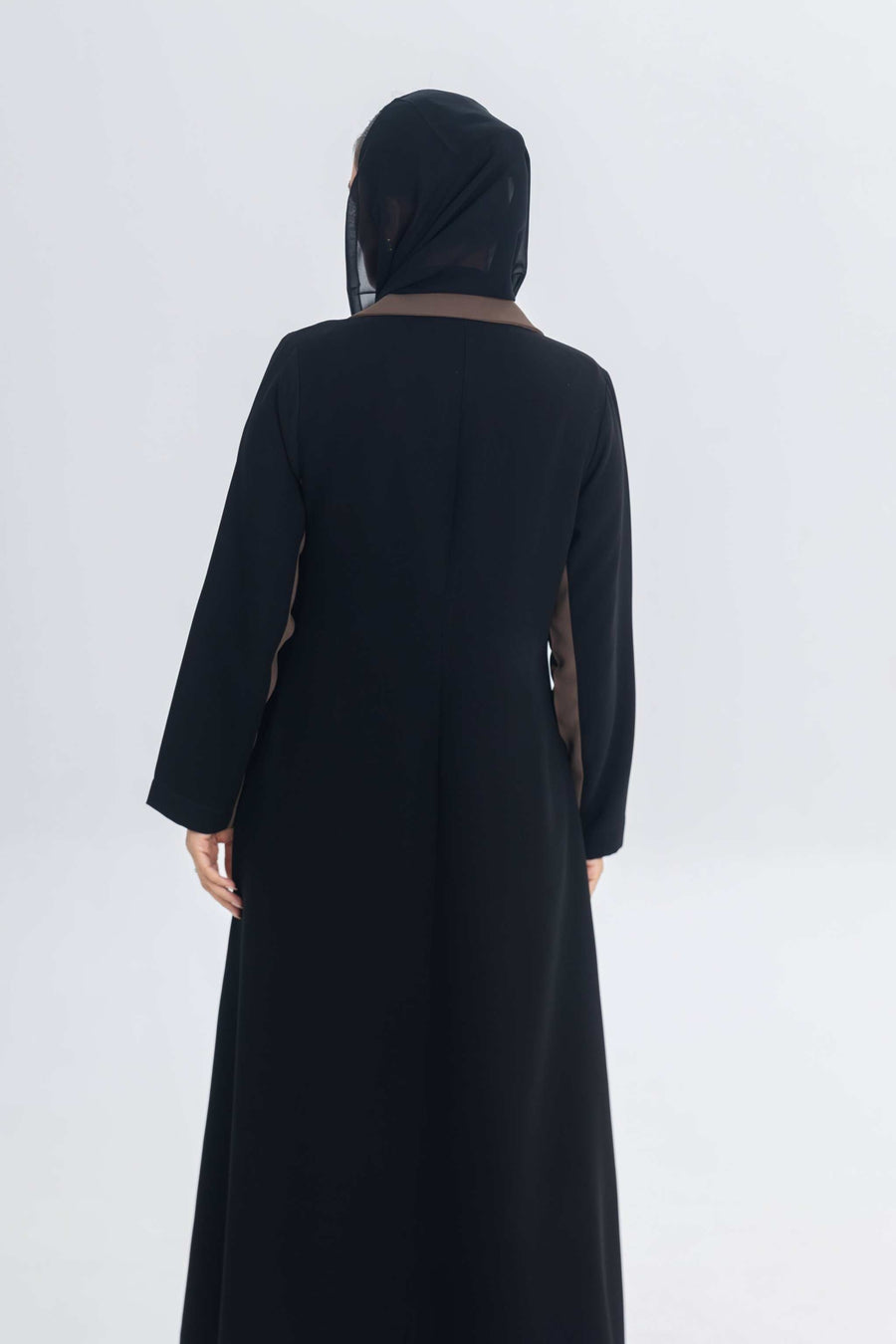Back view of black crepe blazer abaya with chestnut brown trim worn with black headscarf on plain background