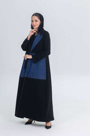 Woman wearing black crepe abaya with denim panels and black hijab standing against white background