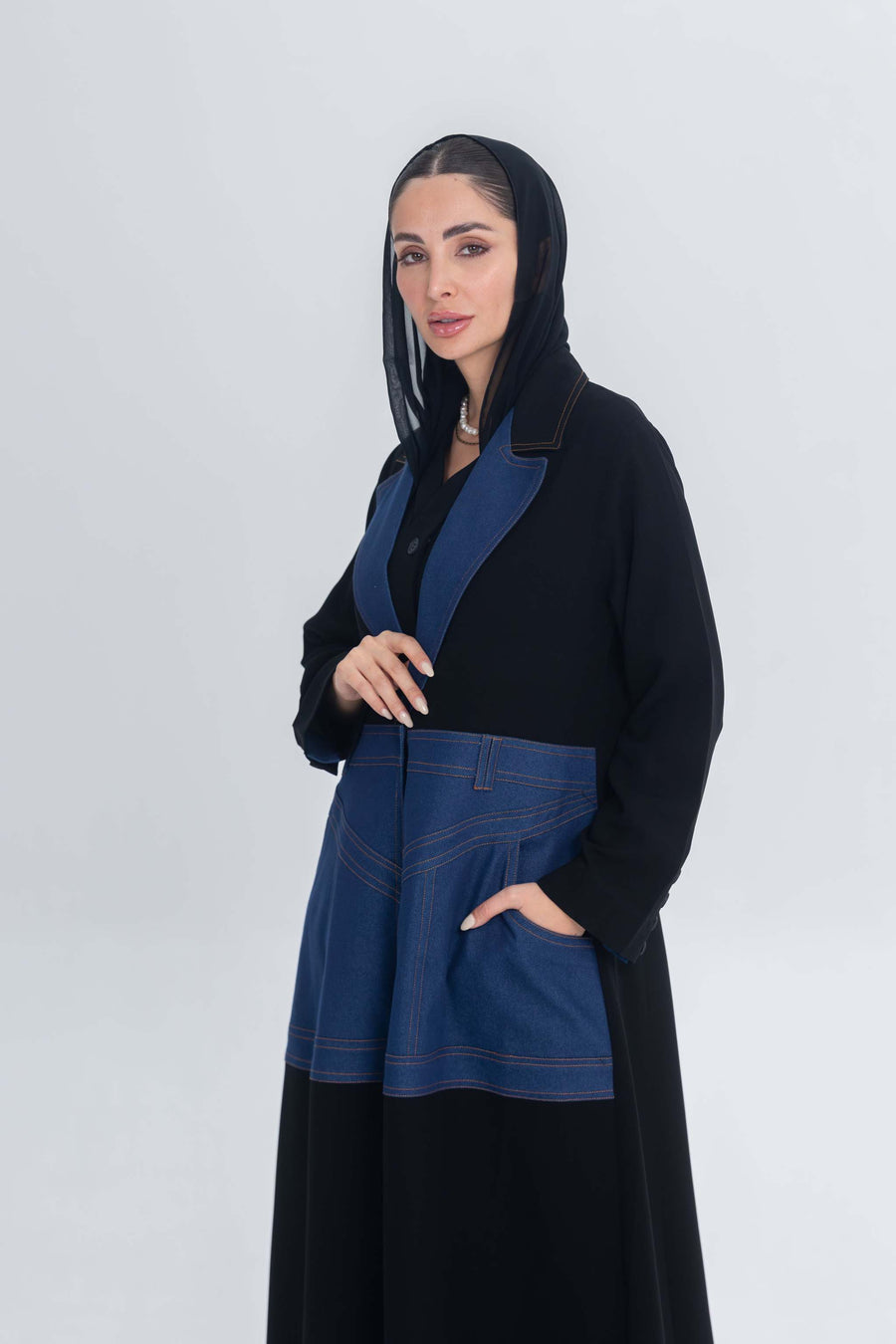Woman wearing a black crepe abaya with blue denim panels and hood, featuring a modern and elegant design.