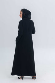 woman wearing black crepe abaya with denim accents standing against plain background