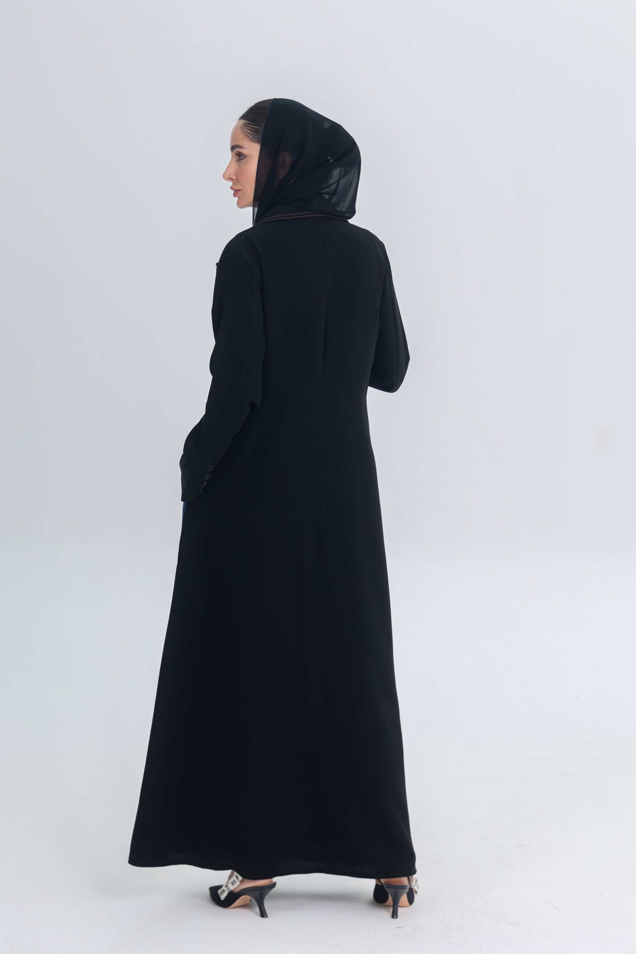 woman wearing black crepe abaya with denim accents standing against plain background