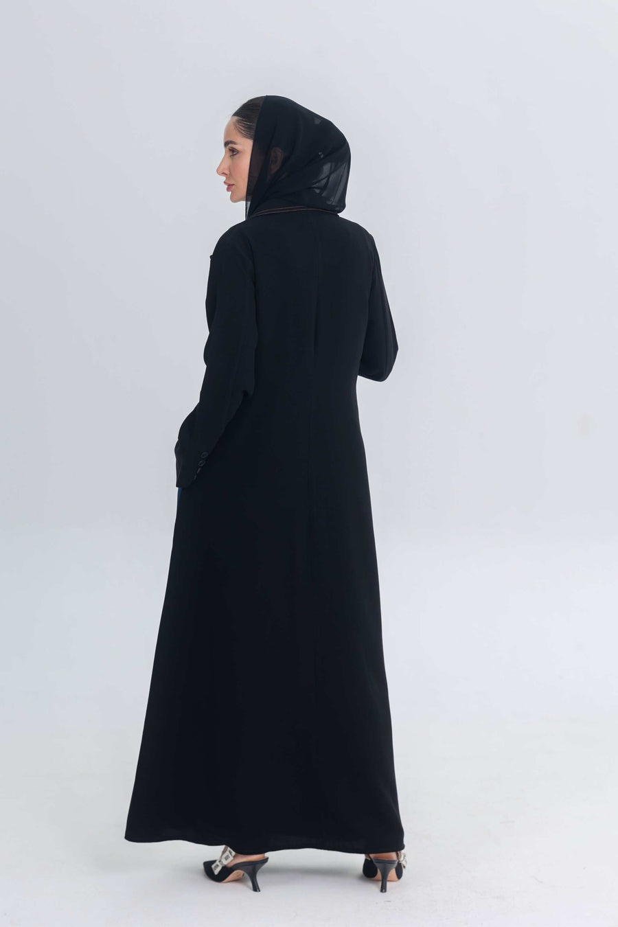 woman wearing black crepe abaya with denim accents standing against plain background