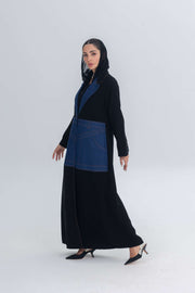 Black crepe abaya with blue denim panels and hood worn by woman in heels against light background