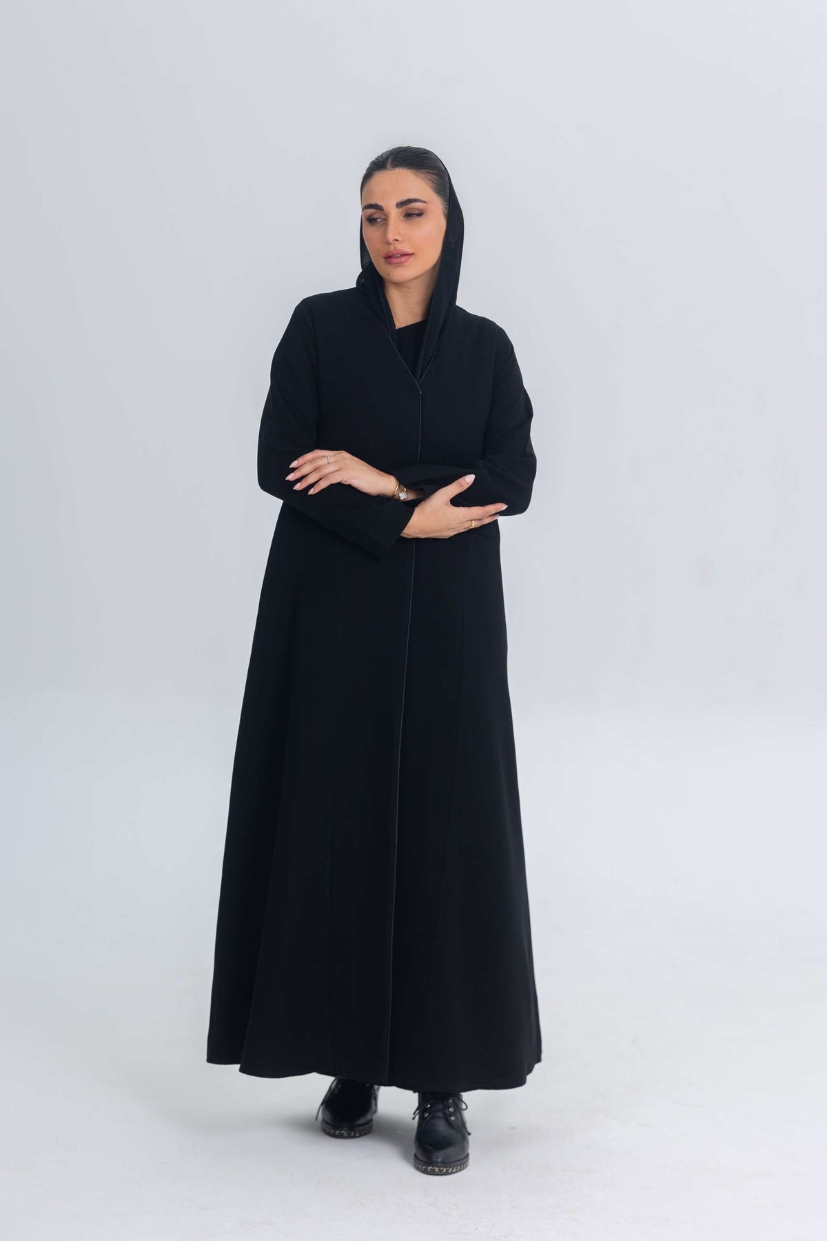 Woman wearing black crepe abaya with subtle satin details, standing against plain background