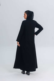 Woman wearing a black crepe abaya with subtle satin detailing, shown from the back.