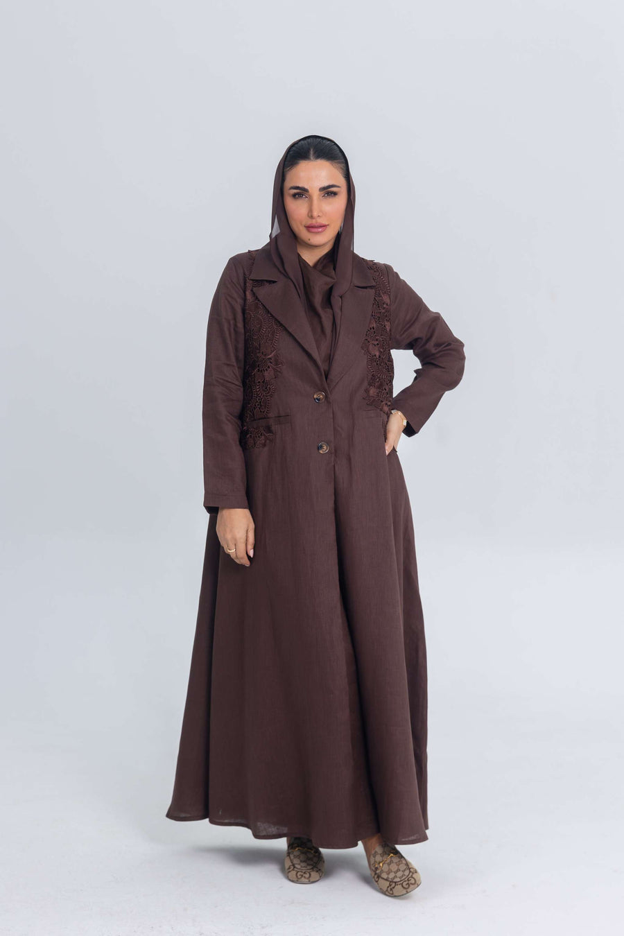 Woman wearing a brown linen abaya with blazer collar and floral lace embroidery patches, designed for lightweight summer wear.