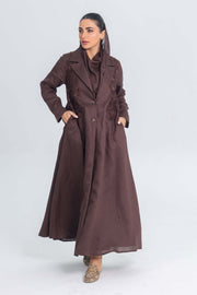 Woman wearing brown linen abaya with blazer collar and floral lace embroidery patches, standing against light background
