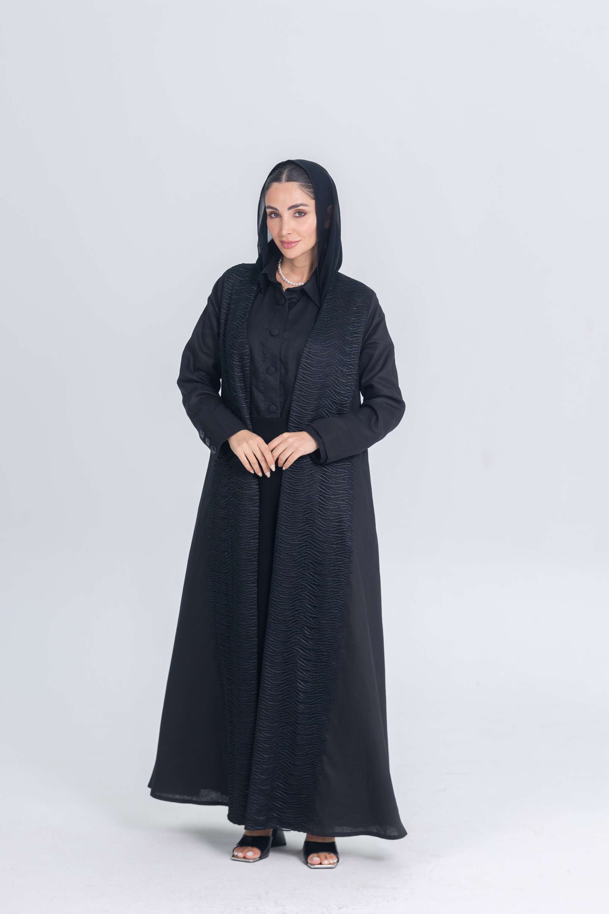 Woman wearing Black Mirage black linen abaya with textured fabric and hood, styled for modest modern elegance
