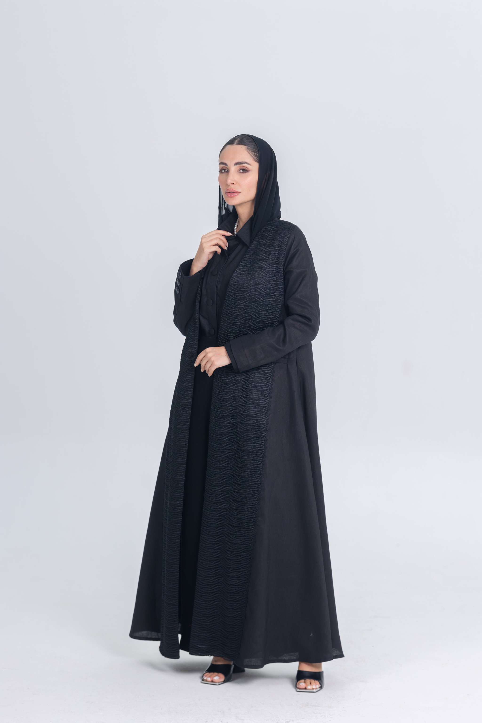 Woman wearing a black linen abaya with textured fabric detail, styled for modern modest wear.