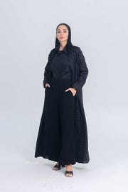 Woman wearing black linen abaya with textured fabric accents and wide-leg pants, styled for modern modest wear