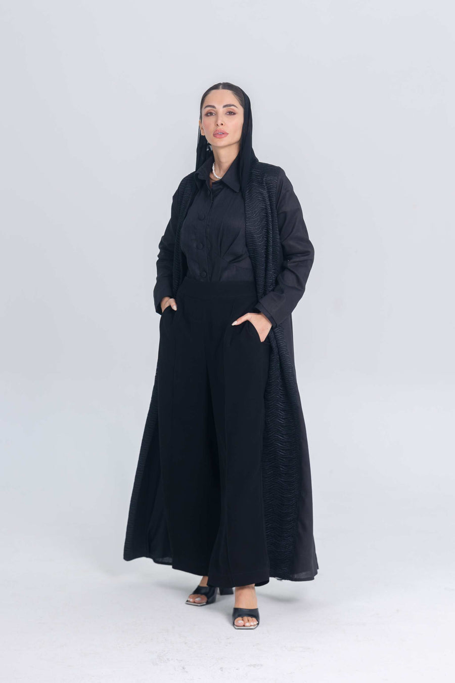 Woman wearing black linen abaya with textured fabric accents and wide-leg pants, styled for modern modest wear
