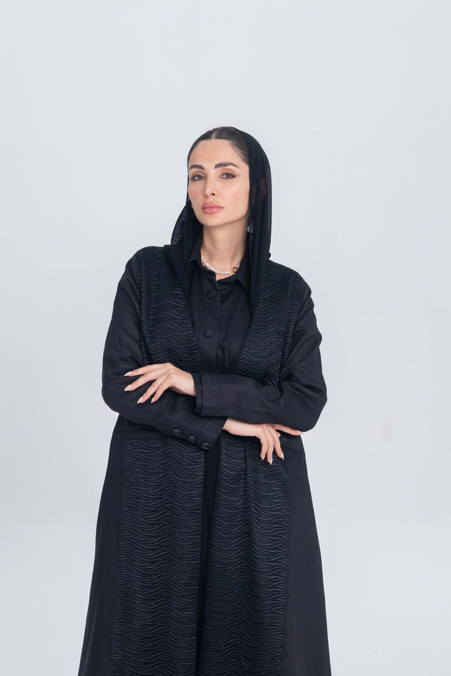 Woman wearing elegant black linen abaya with textured fabric panels and hood against plain background