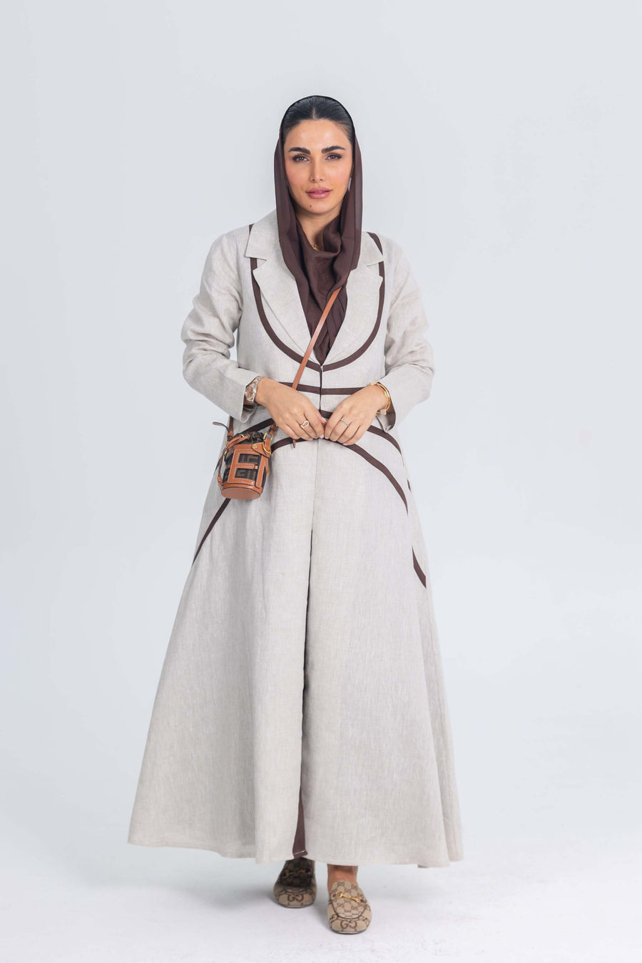 Woman wearing beige linen abaya with brown trim and matching headscarf, carrying a small plaid crossbody bag