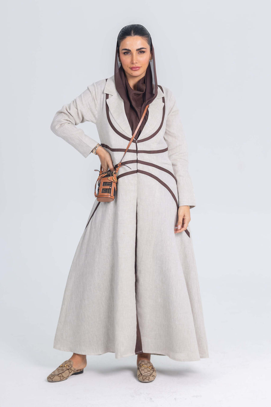 woman wearing beige linen abaya with brown brim and matching brown hijab carrying a small tan crossbody bag