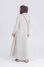 Woman wearing beige linen abaya with brown brim and brown headscarf standing against white background