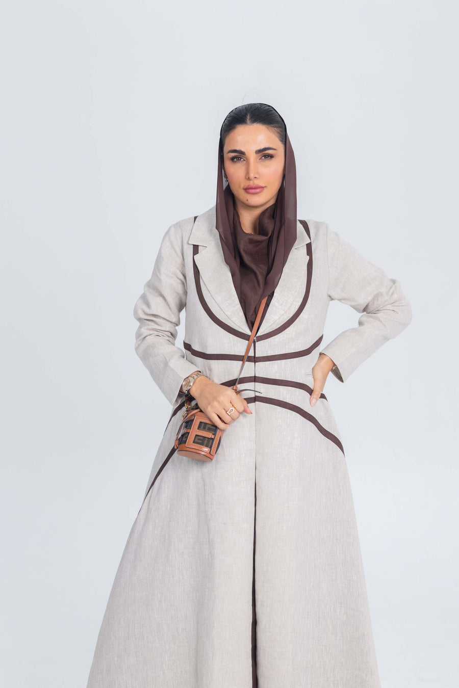 Beige linen abaya with brown trim worn with matching brown hijab and small crossbody bag